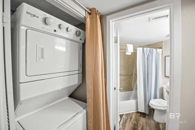 laundry room with stacked washer and dryer, laundry area, visible vents, and dark wood-style flooring