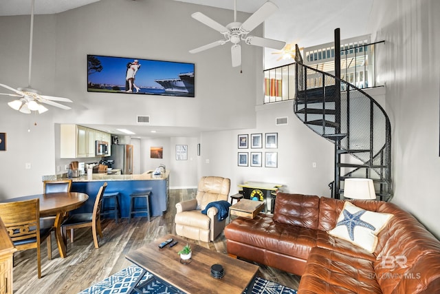 living room featuring high vaulted ceiling, light wood-type flooring, visible vents, and stairs