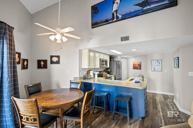 dining space featuring dark wood-type flooring, a ceiling fan, a towering ceiling, visible vents, and baseboards