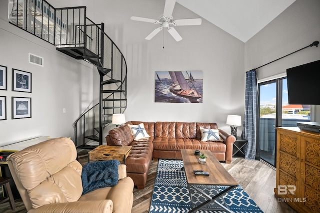 living area featuring ceiling fan, high vaulted ceiling, wood finished floors, visible vents, and stairway