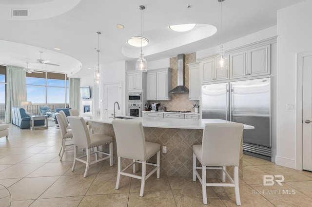 kitchen with wall chimney range hood, appliances with stainless steel finishes, a spacious island, a kitchen breakfast bar, and pendant lighting