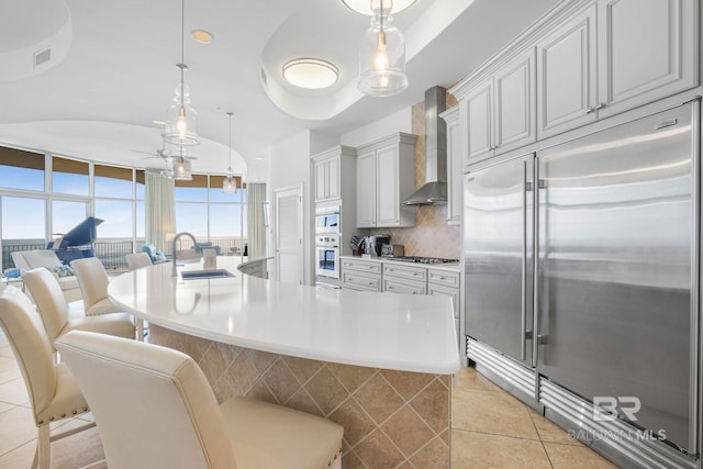 kitchen with stainless steel appliances, wall chimney exhaust hood, sink, and pendant lighting