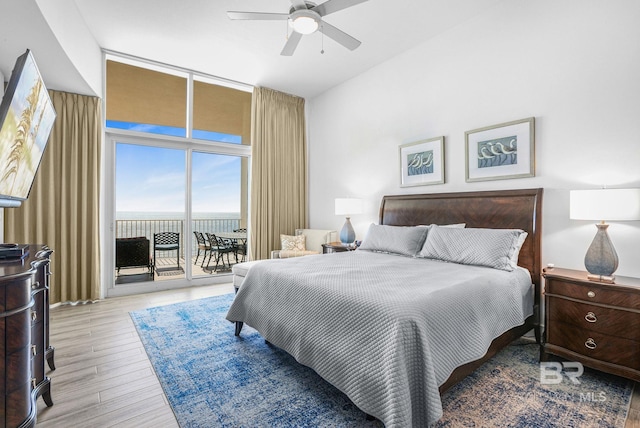 bedroom with access to outside, light hardwood / wood-style flooring, expansive windows, a water view, and ceiling fan