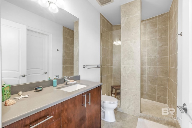 bathroom with vanity, toilet, a tile shower, and tile patterned flooring