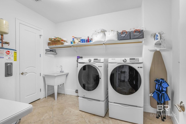 clothes washing area featuring light tile patterned floors, washer and clothes dryer, and water heater