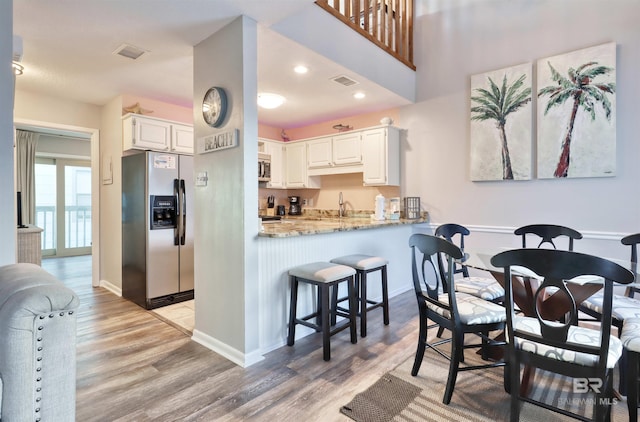 kitchen with kitchen peninsula, light hardwood / wood-style flooring, light stone countertops, appliances with stainless steel finishes, and white cabinetry