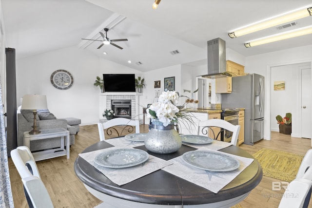 dining space with ceiling fan, a fireplace, lofted ceiling with beams, and light hardwood / wood-style flooring