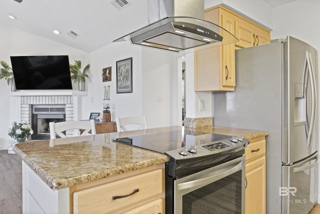 kitchen featuring island exhaust hood, light brown cabinetry, stainless steel appliances, and a brick fireplace