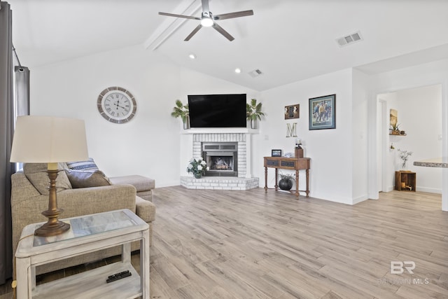 living room featuring vaulted ceiling with beams, ceiling fan, light hardwood / wood-style floors, and a brick fireplace