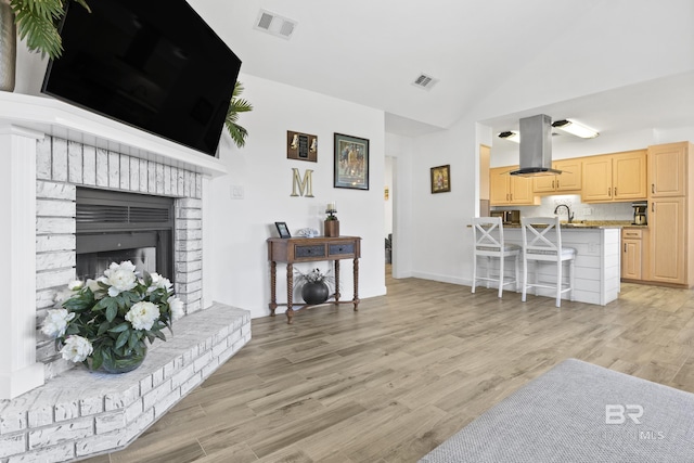 living room with sink, light hardwood / wood-style floors, lofted ceiling, and a brick fireplace