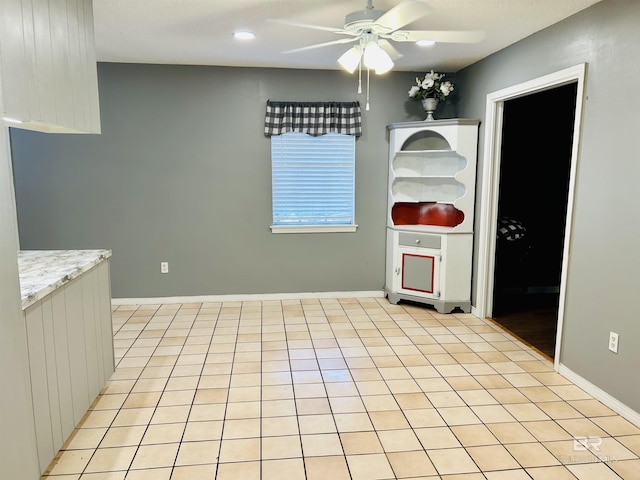 kitchen with light tile patterned flooring, ceiling fan, and light stone counters