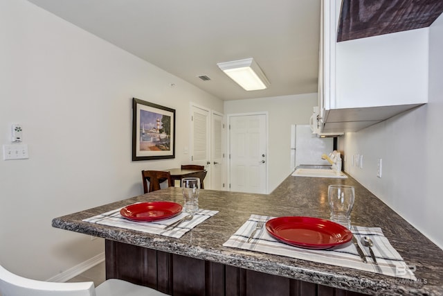 kitchen with a peninsula, a sink, visible vents, freestanding refrigerator, and a kitchen bar