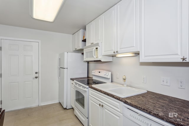 kitchen featuring white cabinets, dark countertops, a sink, white appliances, and baseboards
