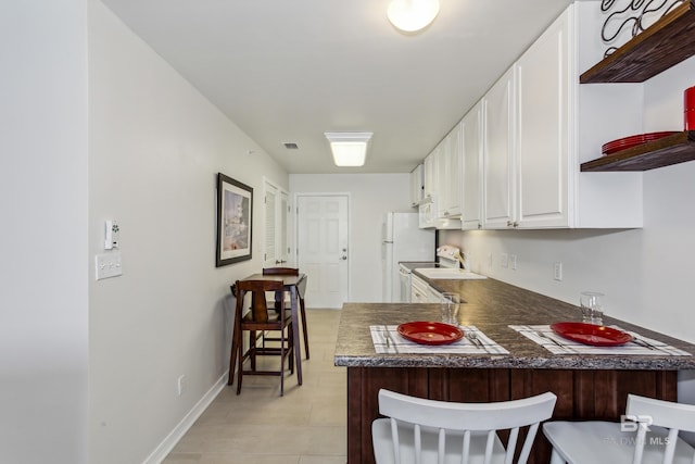 kitchen with white cabinets, a peninsula, baseboards, a kitchen bar, and open shelves