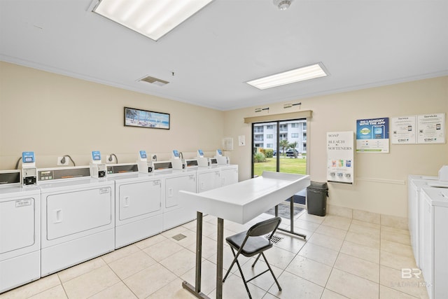 clothes washing area with washing machine and clothes dryer, ornamental molding, and light tile floors