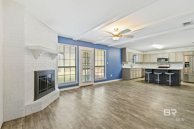 unfurnished living room featuring beamed ceiling, dark hardwood / wood-style floors, ceiling fan, and a fireplace