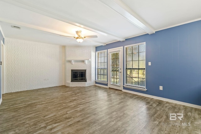 unfurnished living room featuring ceiling fan, beamed ceiling, crown molding, hardwood / wood-style floors, and a fireplace