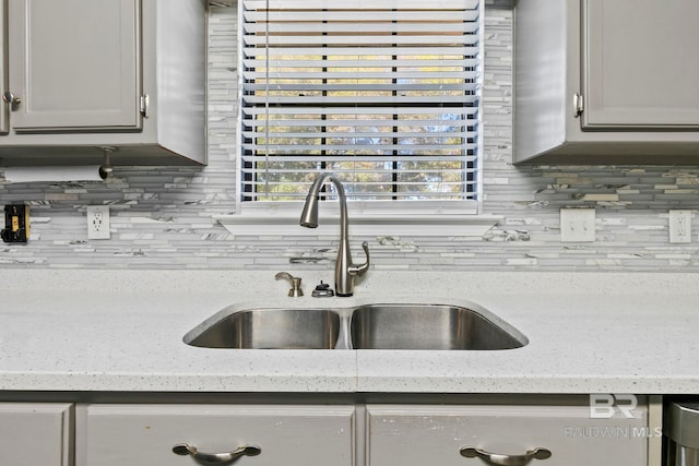 kitchen featuring decorative backsplash, light stone counters, and sink