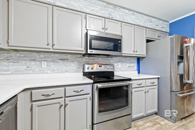 kitchen featuring backsplash, crown molding, gray cabinets, appliances with stainless steel finishes, and light hardwood / wood-style floors