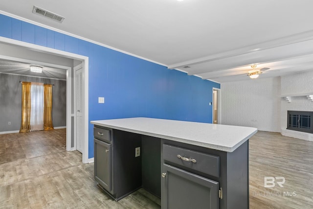 kitchen with a fireplace, ceiling fan, light hardwood / wood-style flooring, beamed ceiling, and a kitchen island