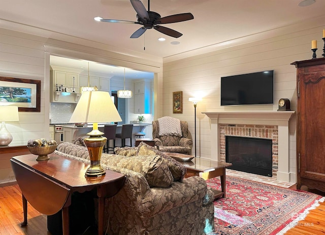 living room with wooden walls, ceiling fan, light wood-type flooring, and a brick fireplace