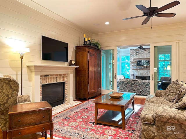 living room featuring hardwood / wood-style flooring, a brick fireplace, wood walls, and ceiling fan