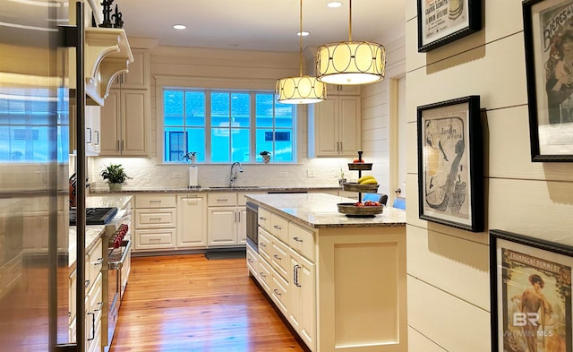 kitchen with light wood-type flooring, light stone counters, stainless steel refrigerator, sink, and pendant lighting