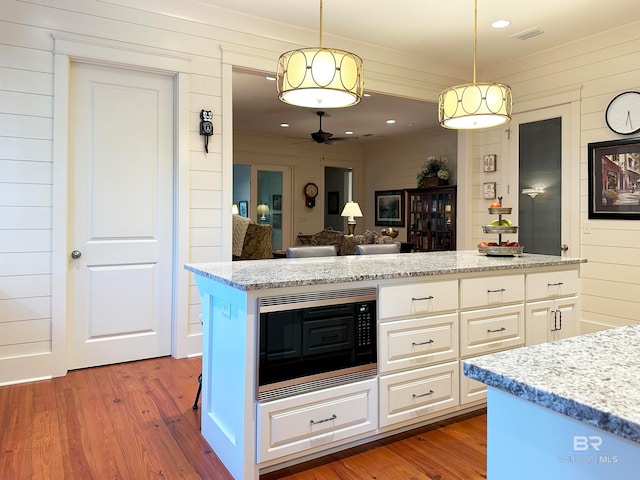 kitchen with hardwood / wood-style floors, wooden walls, white cabinetry, hanging light fixtures, and black microwave