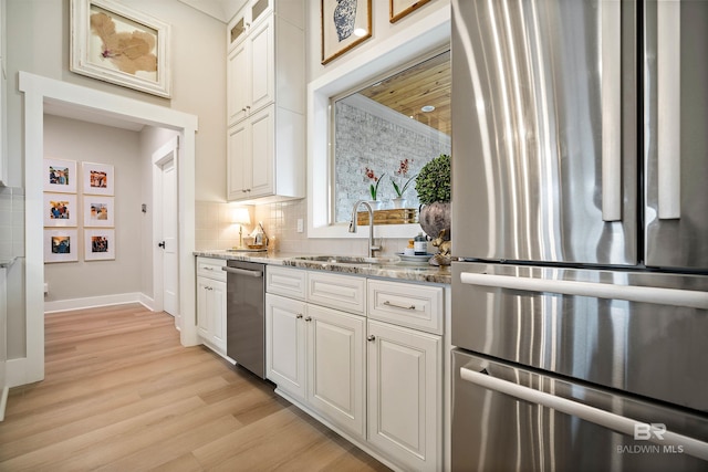 kitchen with white cabinetry, sink, light stone countertops, light hardwood / wood-style floors, and appliances with stainless steel finishes