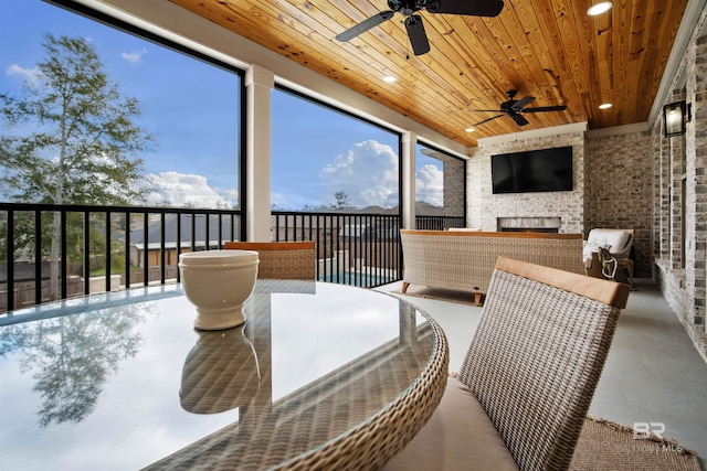 sunroom featuring an outdoor stone fireplace, ceiling fan, and wooden ceiling