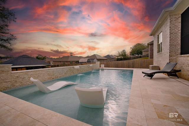 pool at dusk featuring a patio area, pool water feature, and a water slide