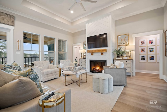 living room with light hardwood / wood-style flooring, ceiling fan, ornamental molding, a towering ceiling, and a fireplace