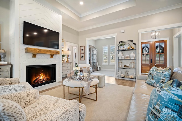 living room featuring light wood-type flooring, a large fireplace, a chandelier, and crown molding