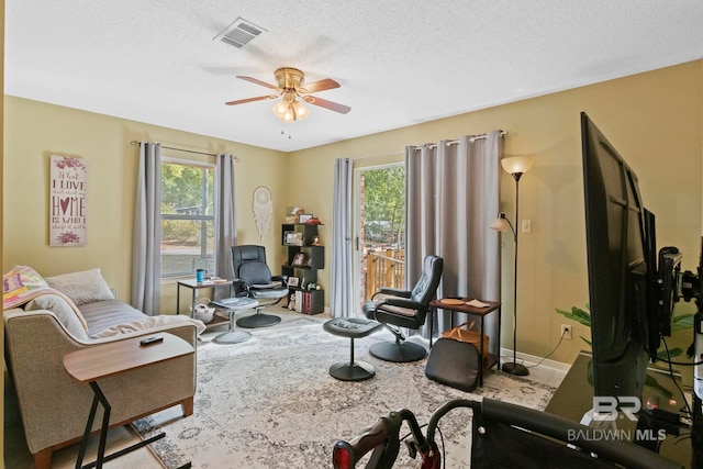 living area featuring ceiling fan, a healthy amount of sunlight, and a textured ceiling