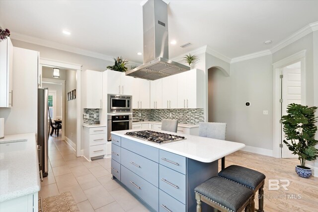 kitchen with a kitchen bar, appliances with stainless steel finishes, tasteful backsplash, island range hood, and white cabinetry