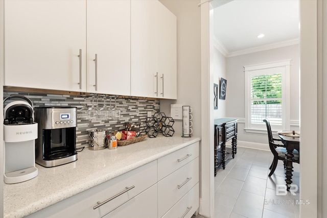 kitchen with white cabinetry, light tile patterned flooring, tasteful backsplash, ornamental molding, and light stone counters