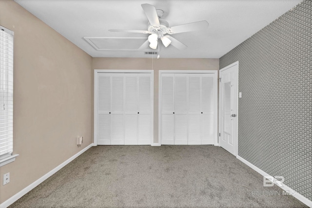 unfurnished bedroom featuring carpet flooring, two closets, and ceiling fan