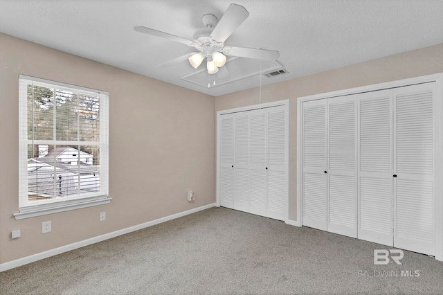 unfurnished bedroom with two closets, carpet floors, a textured ceiling, and ceiling fan