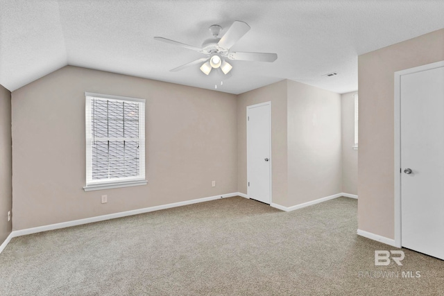 unfurnished room featuring ceiling fan, vaulted ceiling, a textured ceiling, and carpet