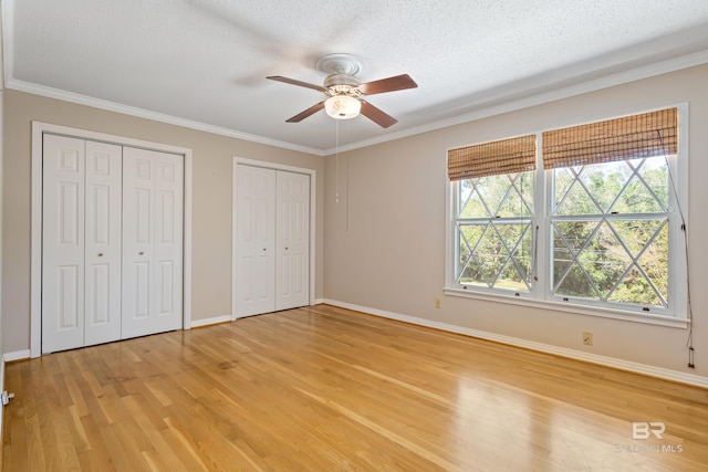 606 Fairhope Ave, Fairhope, AL 36532 - unfurnished bedroom with light wood-style floors, two closets, baseboards, ornamental molding, and a textured ceiling