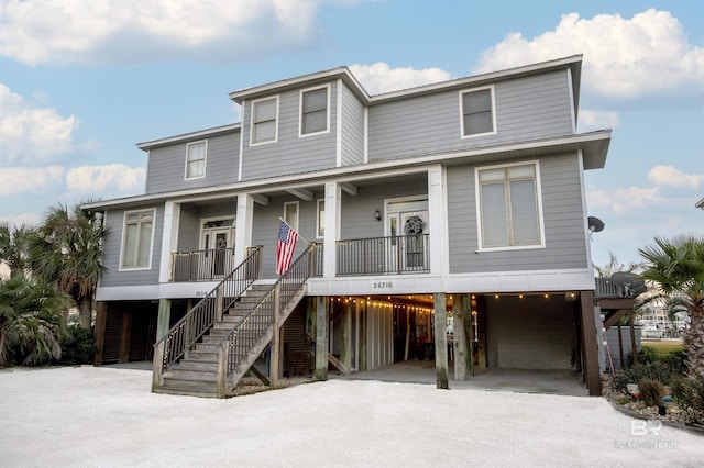 raised beach house featuring a porch, an attached garage, stairs, and driveway