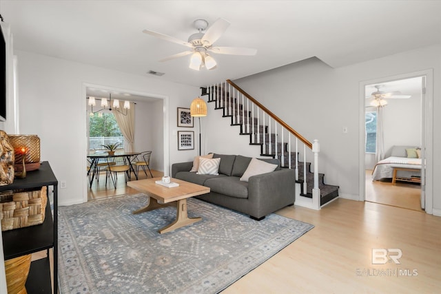 living room with ceiling fan with notable chandelier and light wood-type flooring