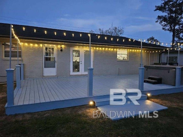 back house at dusk featuring a hot tub and a deck