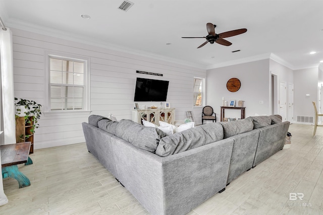 living area featuring a ceiling fan, baseboards, visible vents, light wood-style floors, and crown molding