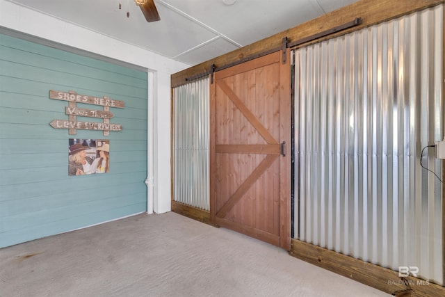 carpeted empty room featuring ceiling fan, a barn door, and wooden walls