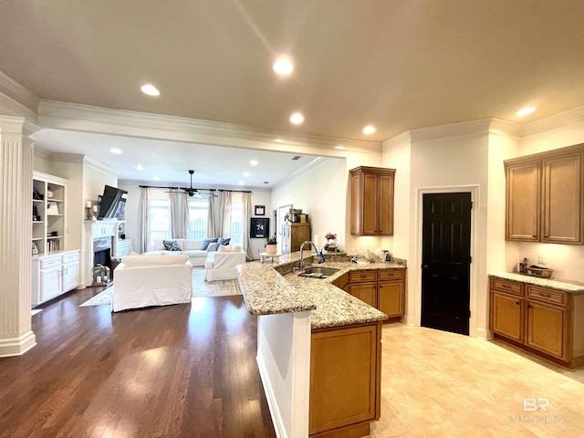 kitchen featuring light stone countertops, open floor plan, brown cabinets, a peninsula, and a sink