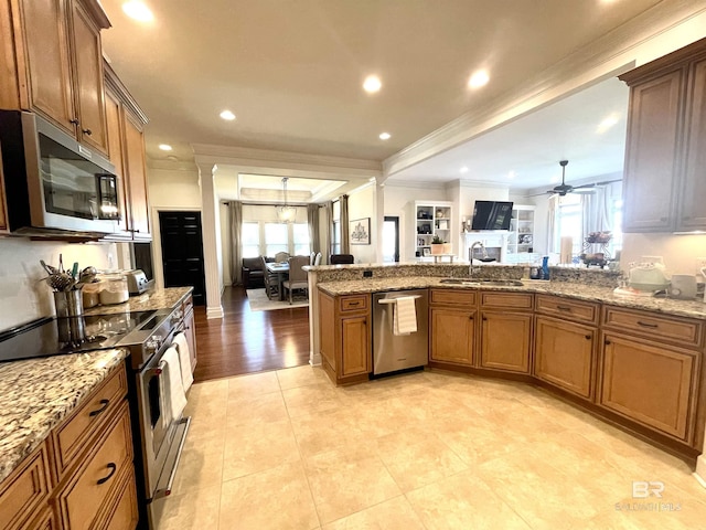 kitchen featuring a sink, open floor plan, appliances with stainless steel finishes, brown cabinetry, and decorative columns