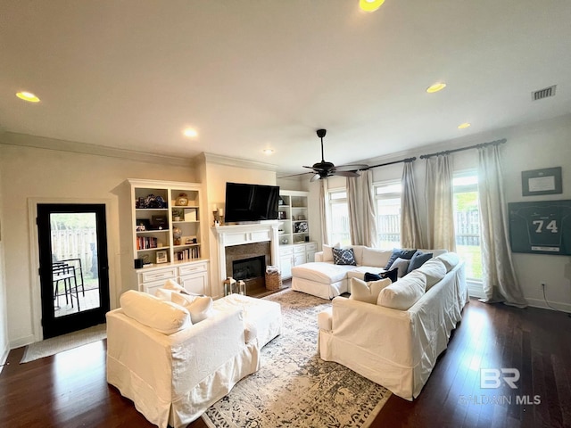 living room with visible vents, dark wood-type flooring, a glass covered fireplace, recessed lighting, and crown molding