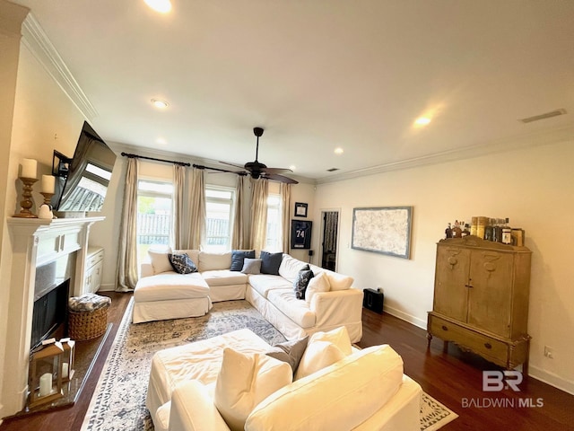 living area featuring dark wood-style floors, visible vents, a fireplace with raised hearth, ceiling fan, and crown molding