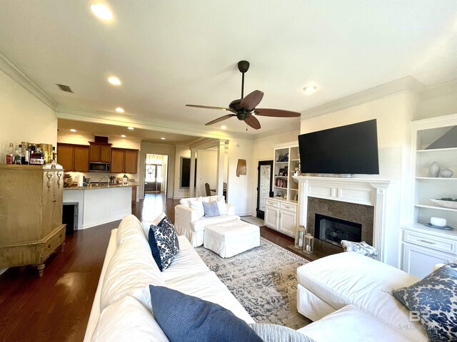 living area with visible vents, recessed lighting, dark wood-style flooring, ornamental molding, and a glass covered fireplace